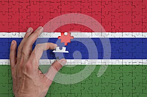 Gambia flag is depicted on a puzzle, which the man`s hand completes to fold