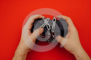 Game addiction concept. Hands of a young man holds a game controller is tied by chain