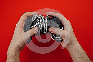 Game addiction concept. Hands of a young man holds a game controller is tied by chain isolated on red background
