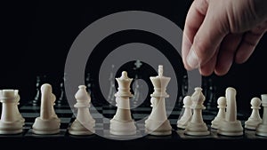 Game of chess. Waiting for the start. Male hand puts a white chess piece pawn on the chessboard on black background. The concept