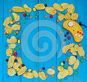 Game controller, chips and candy on a blue wooden background.