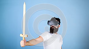 Gamer concept. Guy with head mounted display holds sword, play fighting game in VR. Hipster on serious face enjoy play