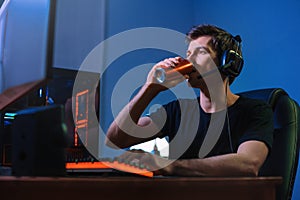 Gamer drinking energy drink to be focused on online computer game at night