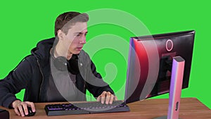 Gamer guy with headphones playing video games on computer and showing thumb up to camera on a Green Screen, Chroma Key.