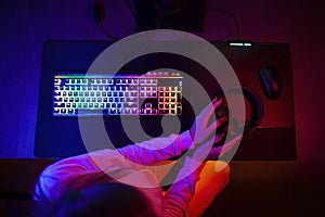 Gamer`s workplace, esports player`s devices, girl`s hands holding headphones in neon lighting