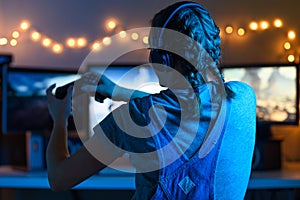 Games online, a young girl playing computer games using a joystick or a gamepad. On three large monitors, creative light.