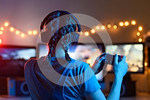 Games online, a young girl playing computer games using a joystick or a gamepad. On three large monitors, creative light.