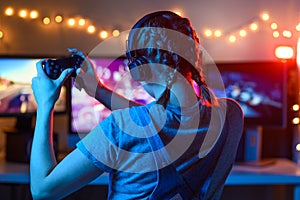 Games online, a young girl playing computer games using a joystick or a gamepad. On three large monitors, creative light.