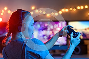 Games online, a young girl playing computer games using a joystick or a gamepad. On three large monitors, creative light.