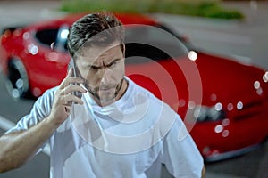 Gangster call phone. Angry man chatting on phone near car on night urban street. Dangerous aggressive man with phone