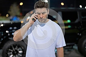 Gangster call phone. Angry man chatting on phone near car on night urban street. Dangerous aggressive man with phone