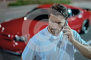 Gangster call phone. Angry man chatting on phone near car on night urban street. Dangerous aggressive man with phone