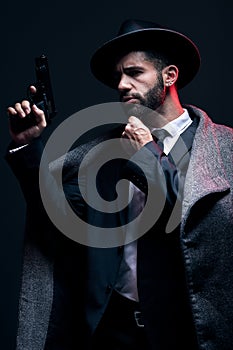 Gangster, leadership or holding gun on studio background in dark secret spy, isolated mafia or crime lord security