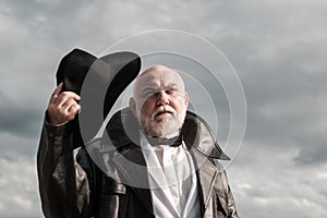 Gangster style. Close up outdoor portrait of serious stylish fashion old mature senior in leather coat and fashion hat