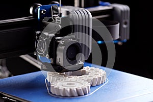 gantry with x-carriage and print head of a FDM-3D-printer that produces white helical gears on blue print bed photo