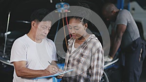 Garage businessman talking explain to car owner about check list service price detail with engine mechanic working in background
