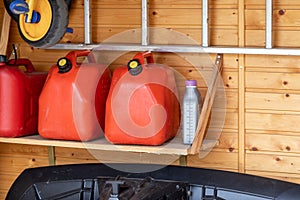 Garage corner with three red plastic fuel cans , staircase and snow plough for atv with wooden wall on background. Petrol gas