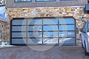 Garage door with glass panes reflecting a snowy hill landscape under blue sky