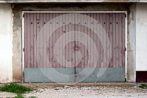 Garage doors made of dilapidated wooden boards with metal plate rain protection mounted on cracked old wall