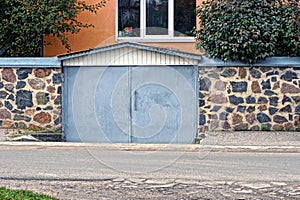Garage with gray metal gates and a stone fence on the street
