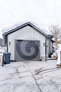 Garage of home with snowy gable roof and dark gray door against cloudy sky view