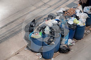 Garbage against full trash cans with rubbish bags overflowing on