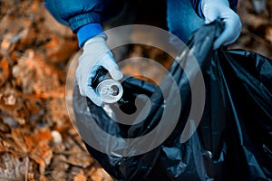 A garbage bag and a crumpled soda can. Girl cleans up in the forest in autumn