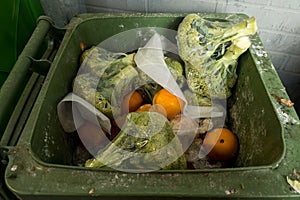 Garbage cans with rotting broccoli and vegetables in plastic packaging near a grocery store