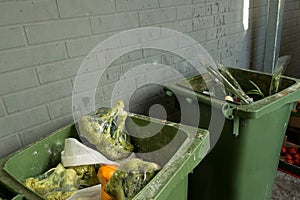 Garbage cans with rotting broccoli and vegetables in plastic packaging near a grocery store