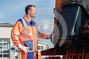 Garbage collection worker putting bin into waste truck photo