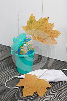 Garbage container with a globe. Nearby is a protective mask for a pandemic and dried maple leaves