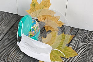 Garbage container with a globe. Nearby is a protective mask for a pandemic and dried maple leaves