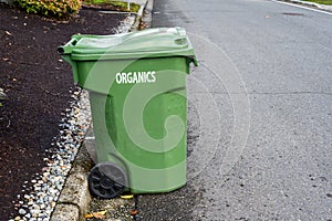 Garbage day, large plastic green yard waste bin sitting out at the curb, recycling of organics and yard waste