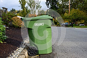 Garbage day, large plastic green yard waste bin sitting out at the curb, recycling of organics and yard waste