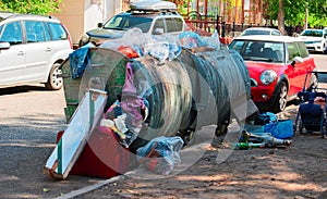 Garbage overfilled trash dumpsters in the street, surrounded by expensive cars