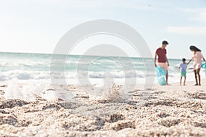 Garbage on sand with multiracial family cleaning beach on sunny day against sky with copy space