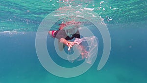 garbage in the sea. Volunteer, girl teenager, in snorkeling mask, collects floating rubbish over the coral reef