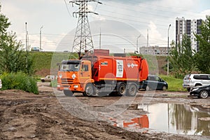 A garbage truck with an inscription in Russian on its body - Recycling Company, drives around a puddle in a residential