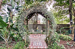 Garden archway overed with green folage onto red brick patio photo