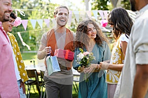 Garden birthday party with surprise. Friends holding birthday gifts and flowers. Family garden gathering during warm