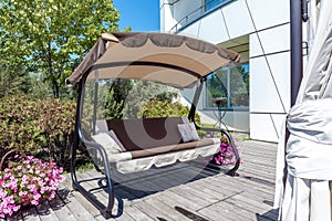 Garden canopy swing bench on wood paved patio area in country estate garden in summer