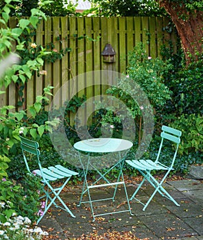 Garden chairs and table in a relaxing, serene, peaceful, lush and private home backyard in summer. Green metal patio