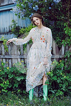 Garden of Eden. Flowers around girl in grey dress and green boots. Portrait of a young attractive girl in long dress sunny summer