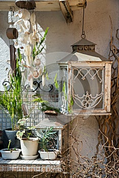 Garden exterior in a rustic style with a dream catcher, lantern and green plants in clay pots. Detail.
