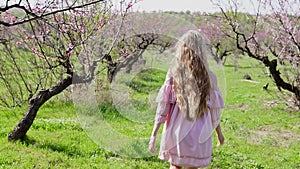 In the garden of flowering trees goes blonde girl in pink dress