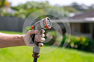 Garden hose with nozzle. Man\'s hand holding spray gun and watering plants, spraying water on grass in backyard