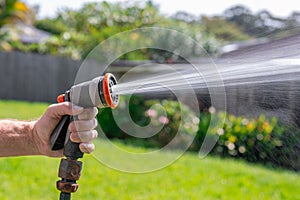 Garden hose with nozzle. Man\'s hand holding spray gun and watering plants, spraying water on grass in backyard