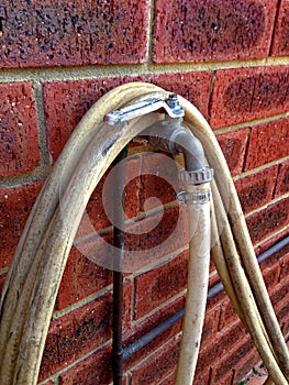 Garden hose wrapped around tap on brick wall