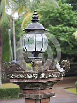 A garden lamp with a vintage design is placed on a brownish red stone pillar