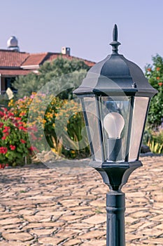 Garden lantern in traditional European rural courtyard with house and flowering plants on background